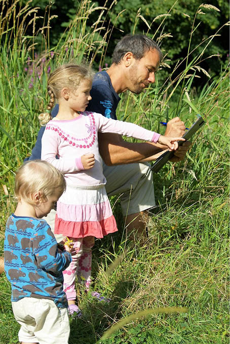 Ein Mann und zwei Kinder kartieren inmitten einer Wiese - Foto: Imke Dirks